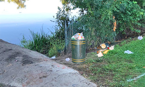 Cleanup site with trash scattered on grass near garbage can